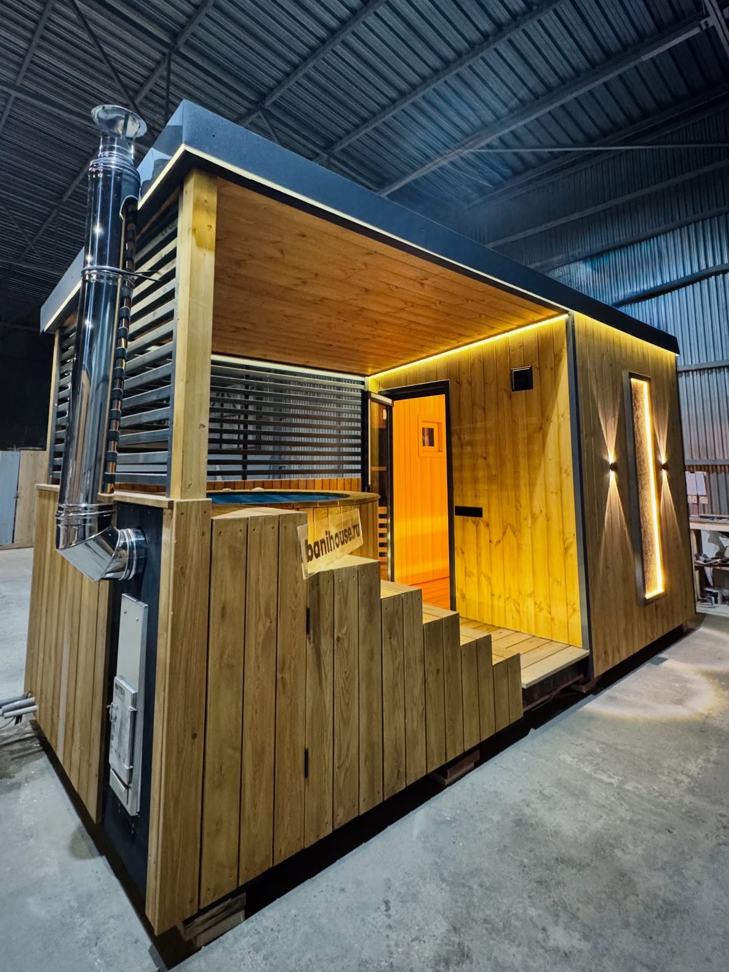 Она безупречна 😍
Баня 5,5 на 2,5 метра с купелью. 
▫️ Купель глубиной 1,5 метра, обшитая лиственницей, оснащена удобной лестницей с атмосферной подсветкой.
▫️ Над купелью расположен стильный навес, который не только защищает от непогоды, но и добавляет элегантности. 
▫️ Фасад бани украшен панно из можжевельника, дополненным фирменной подсветкой, что придаёт бане особый шарм и индивидуальность. 
▫️ Панорамное окно в парной, расположенное на торце бани, открывает захватывающий вид и наполняет помещение уютным светом, гармонично сочетаясь с топкой печи. 
▫️ Внутри парной находится печь Harvia, окружённая панно из можжевельника и вставками из гималайской соли, создающими уникальную атмосферу расслабления; дополнительно предусмотрены подсветка и краник для подачи воды, что делает это место идеальным для отдыха и восстановления сил.

Стоимость бани от 980.000₽